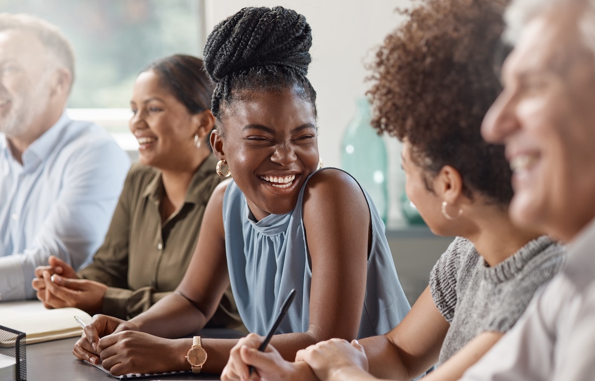 A young African-American woman at a conference table with a broad, genuine smile.